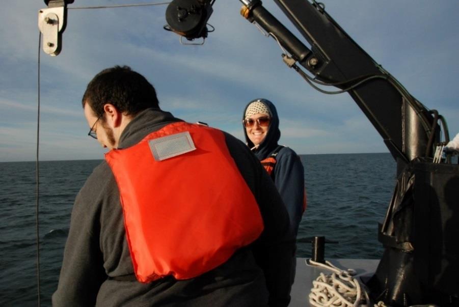 Two individuals in life vests standing beside a crane boom on a boat deck