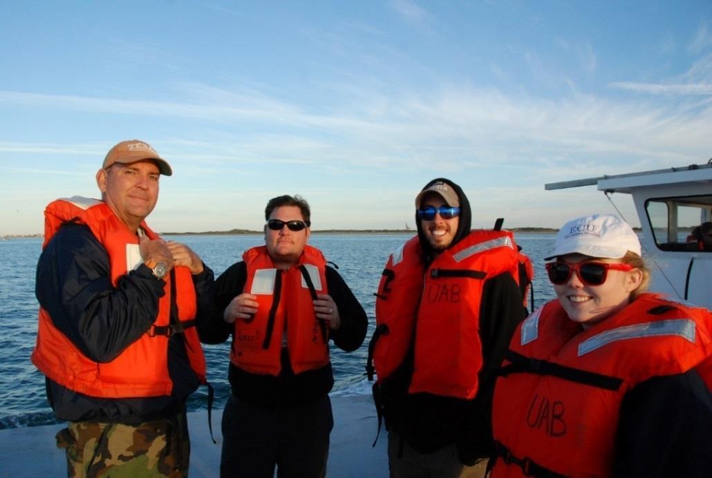 Four crew members in cold weather gear and life jackets posing on a boat deck