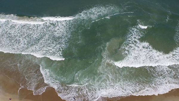 A rip current pulling water out into the ocean with breaking waves on either side