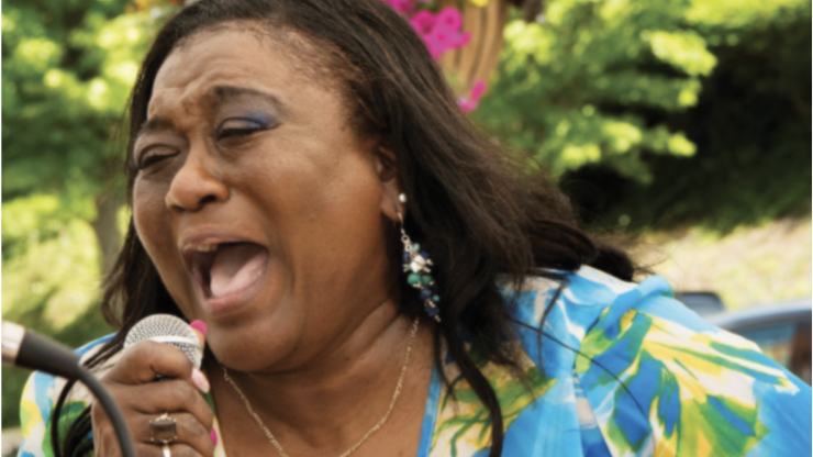 Gospel singer, Mary D. Williams, singing and holding a microphone outside. 