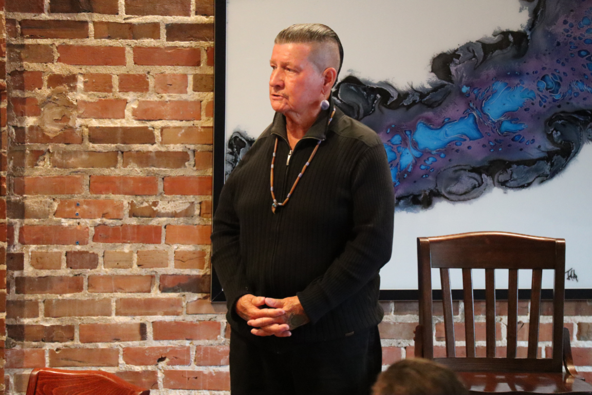 Gray Parsons, older Indigenous man looking to the side in front of a brick wall.  