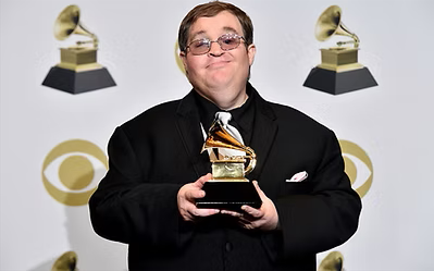 Micheal Cleveland with a Grammy Award in his hands on a red carpet setting. 