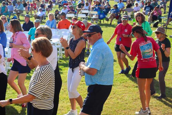 People dancing in a field in mostly red, white and blue attire. Atmosphere is happy with lots of people in the background.