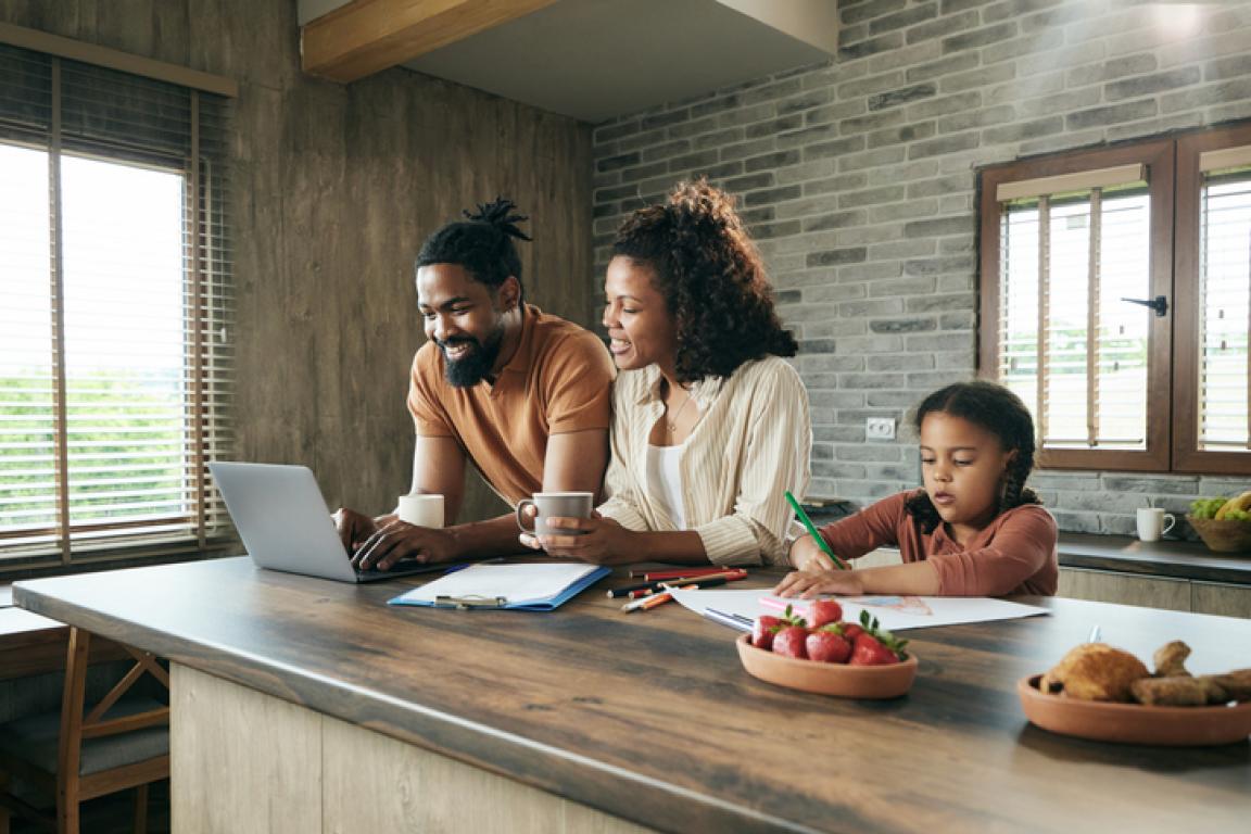 Smiling couple looking at computer while daughter draws beside them, cropped version