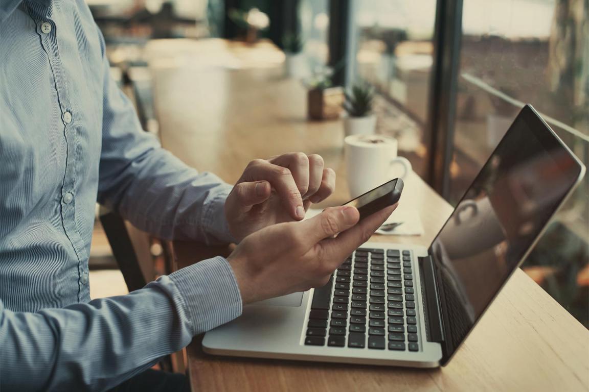 Image of man looking at cell phone and laptop in coffee shop