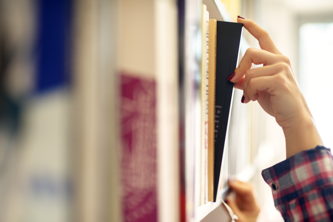 A hand is pulling a book off a shelf at the library. 