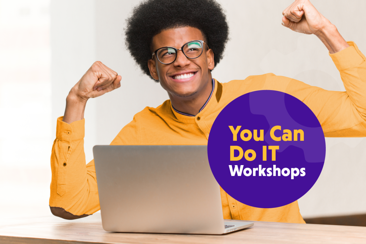 Young man with glasses and yellow shirt flexing in front of an open laptop.